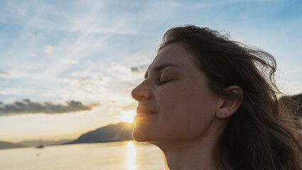 Close up profile portrait of a smiling young woman with closed eyes enjoying sunset on the beach. © olezzo