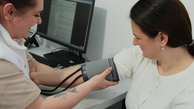 Nurse places blood pressure monitor cuff onto mature woman arm in clinic. Happy doctor examines female patient in hospital slow motion