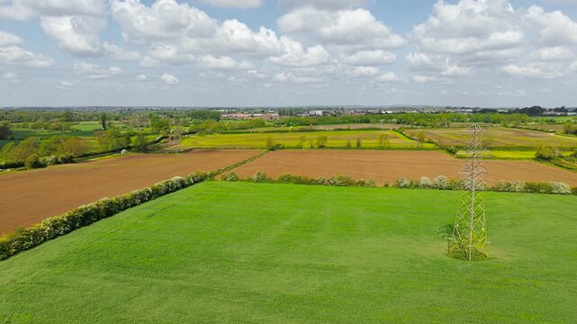 Drone view of cultivated farmland with power infrastructure crossing planted crop fields. Productive arable land and prepared soil parcels. Agriculture management, land development, energy and farming