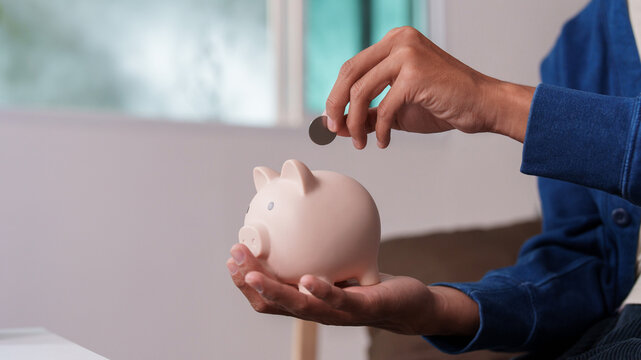 Asian man putting coin into piggy bank for future savings