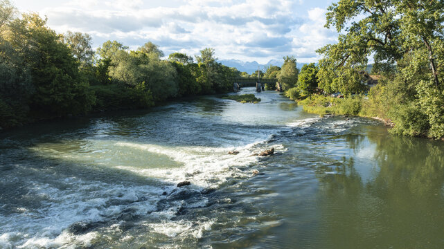 Aerial view of the flowing river with white water rapids, lush green forests on the banks, and distant mountains under a bright sky in Ljubljana, Ljubljana, Slovenia.