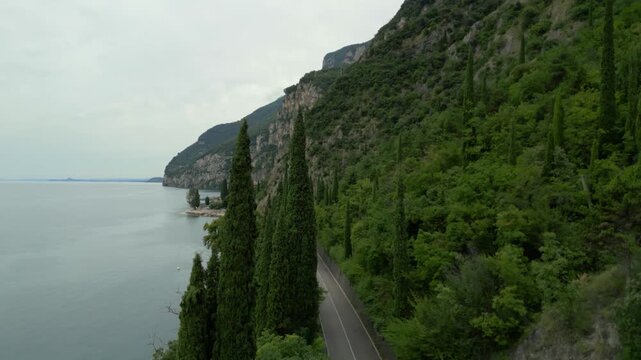 A winding road runs along a lush green hillside beside lake water and rocky cliffs
