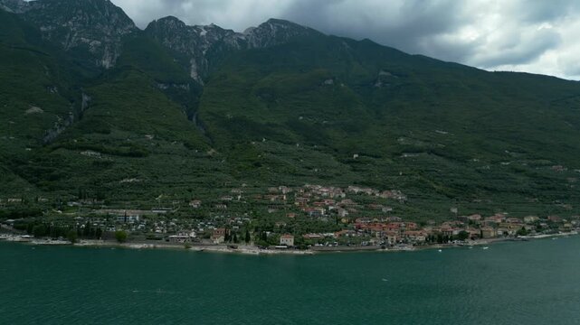 Wide aerial view of Malcesine town on Lake Garda shore beneath Monte Baldo slopes