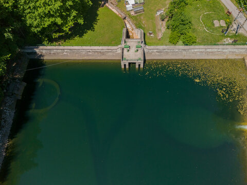 Aerial view of Dolny Jelenec water dam with dark green water and concrete structures surrounded by lush forest in Stare Hory, Banskobystricky kraj, Slovakia.