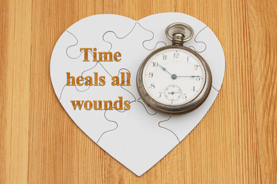 Time heals all wounds text on a white puzzle heart with antique pocket watch on wood for time to heal