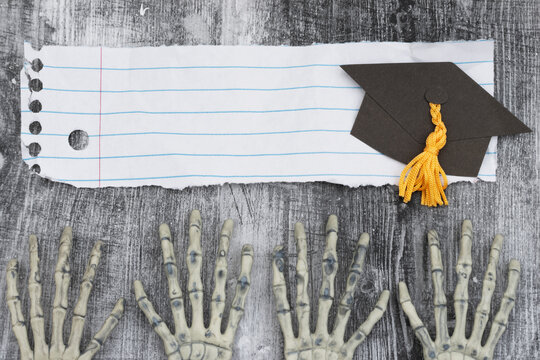 Two pairs of skeleton hands on with ripped paper and grad cap weathered wood