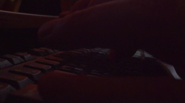  Close up of  hands typing on keyboard in dark room, low key lighting, cinematic coding background.