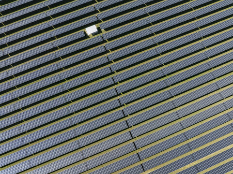Aerial view of rows of solar panels in a large photovoltaic power station with a small white maintenance building Germany.