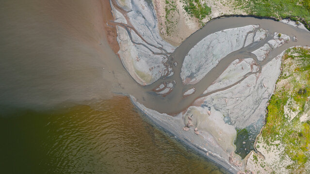 An aerial view of the mouth of a river or stream where it flows into a lake or the sea. A drone shot of the muddy water and the shoreline.