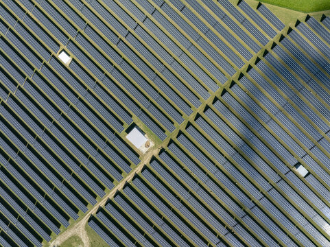 Aerial view of a large solar farm with rows of blue photovoltaic panels and green grass Germany.