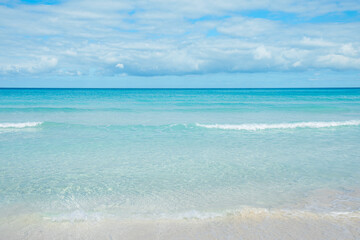 Obraz premium Calm ocean waves gently lap on the sandy shore under a bright blue sky