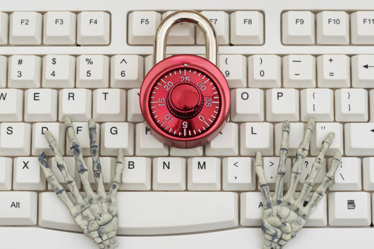Skeleton hands with combination lock on a white computer keyboard for cybersecurity