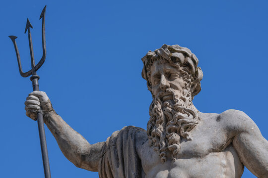 Powerful Neptune holding trident against deep blue sky.