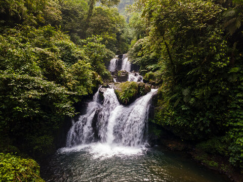 Aerial view of Ambyar waterfall cascading through lush tropical forest and green foliage in Purwokerto, Central Java, Indonesia.