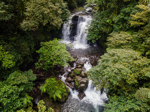 Aerial view of Ambyar waterfall cascading through dense tropical jungle and lush green foliage over dark volcanic rocks in Purwokerto, Central Java, Indonesia.