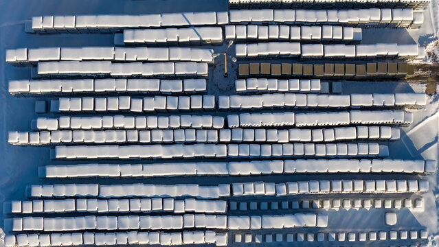 Aerial view of rows of industrial pallets covered in thick white snow with long shadows in an outdoor storage area in Warszawa, Wojewodztwo mazowieck, Poland.