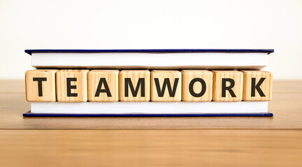 Obraz premium Teamwork word symbol. Concept word Teamwork on beautiful wooden blocks in beautiful book. Beautiful wooden table white background. Business support help teamwork word concept. Copy space.