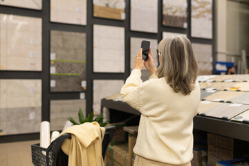 Obraz premium Woman shopping for new tiles, taking a picture with a smartphone for interior design planning