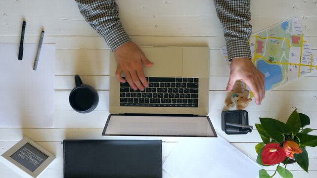 Male arms of businessman typing text on laptop keyboard at wooden desk. Man taking break and playing with his favorite soft toy. Top view on workplace of office employee. Above shot Slow mo Close up