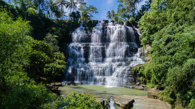 Aerial view of Cigangsa Waterfall cascading down tiered rock formations surrounded by lush tropical forest and palm trees Sukabumi, West Java, Indonesia.