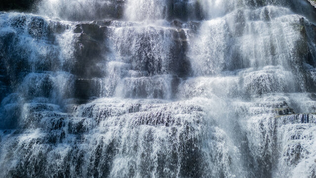 Aerial view of Cigangsa Waterfall with water cascading over tiered dark rock formations and misty spray in Sukabumi, West Java, Indonesia.