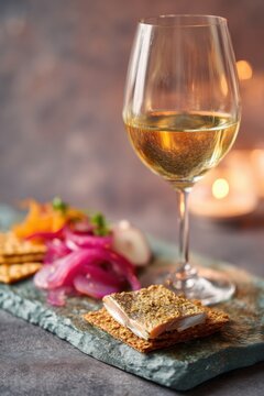 Glass of white wine served with crispy cracker and pickled fish appetizer. Rustic food styling on a stone board for a gourmet dinner party. Elegant restaurant dining concept.