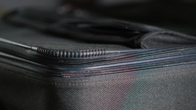 Close up view of hand opening and closing zipper on black soft shell luggage suitcase during travel preparation.