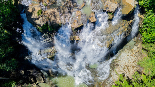 Aerial view of Cigangsa Waterfall cascading over rocky cliffs and surrounded by lush tropical forest in Sukabumi, West Java, Indonesia.