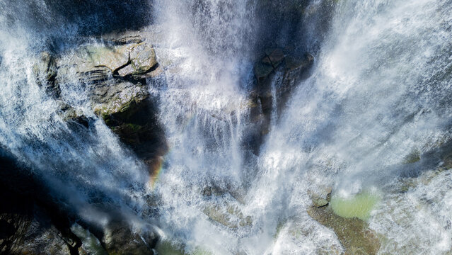 Aerial view of Cigangsa Waterfall with cascading water over dark rocks and a faint rainbow in the mist in Sukabumi, West Java, Indonesia.