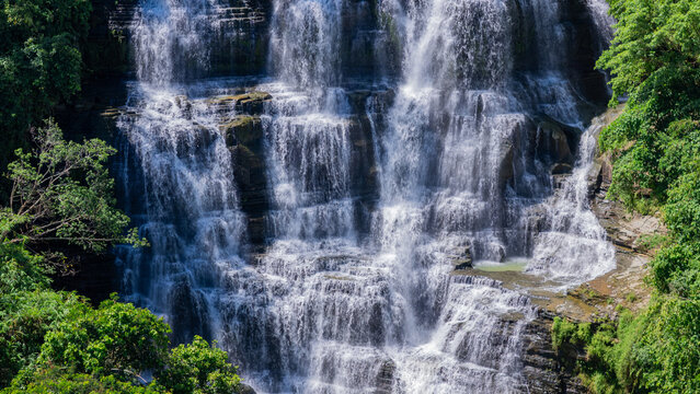 Aerial view of Cigangsa Waterfall featuring multi-tiered cascades flowing over dark layered rock formations and surrounded by lush green trees Sukabumi, West Java, Indonesia.