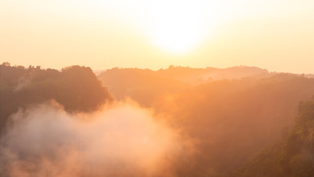 Aerial view of misty tropical hills and lush forest canopy under a golden sunrise glow in Sukabumi, West Java, Indonesia.