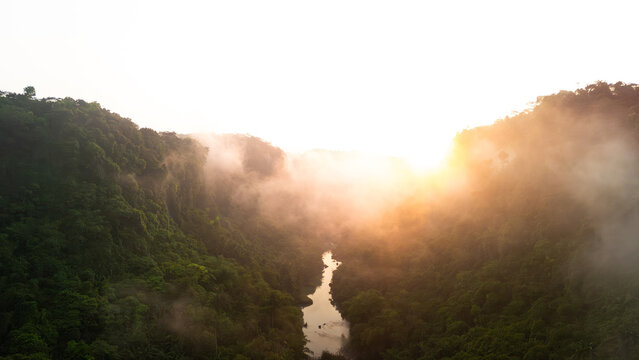 Aerial view of a winding river flowing through a lush tropical valley shrouded in morning mist at sunrise Sukabumi, West Java, Indonesia.