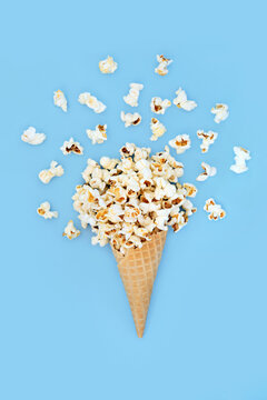 Surreal summer popcorn ice cream cornet on blue background with loose corn. Fun holiday summertime food art whimsical design.