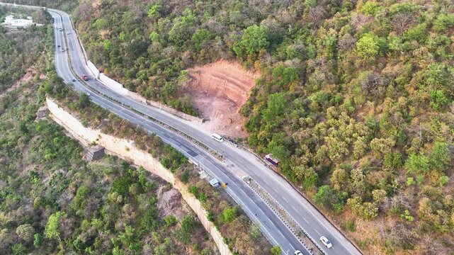 Drone shot of mountain excavation and road widening on highway. Video shows heavy excavation of a steep, forested hillside directly alongside a major national highway in Jammu, India.
