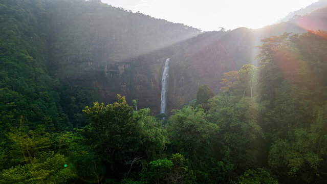 Aerial view of Cikanteh Waterfall cascading down a steep cliff surrounded by lush tropical forest and morning sunlight rays Sukabumi, West Java, Indonesia.