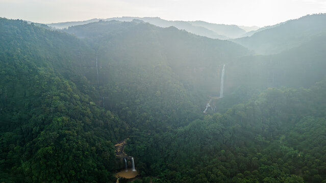 Aerial view of Cikanteh Waterfall cascading down a lush green cliff surrounded by dense tropical forest and misty mountains in Sukabumi, West Java, Indonesia.