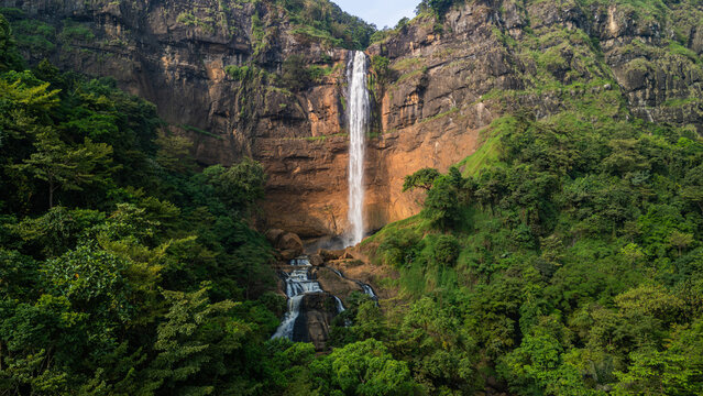 Aerial view of Cikanteh Waterfall cascading down a massive rocky cliff surrounded by lush tropical rainforest Sukabumi, West Java, Indonesia.