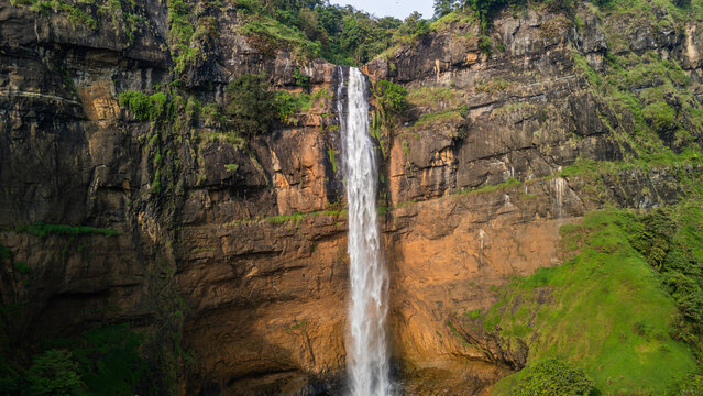 Aerial view of Cikanteh Waterfall cascading down a massive rocky cliff surrounded by lush tropical greenery Sukabumi, West Java, Indonesia.