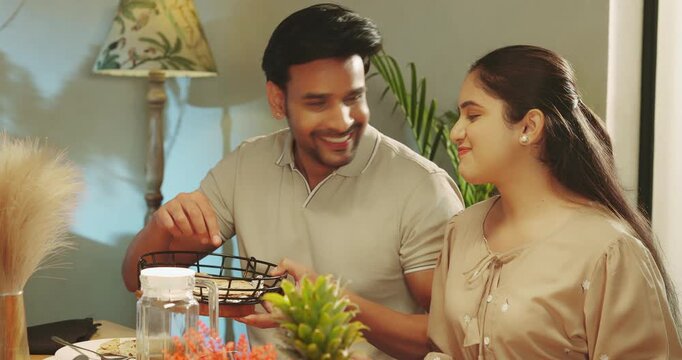 Indian happy man woman couple sitting around table chair talk speak share gossip room place young adult gen z male hold roti bowl serve fresh salad female eat tasty food spend time enjoy dinner night