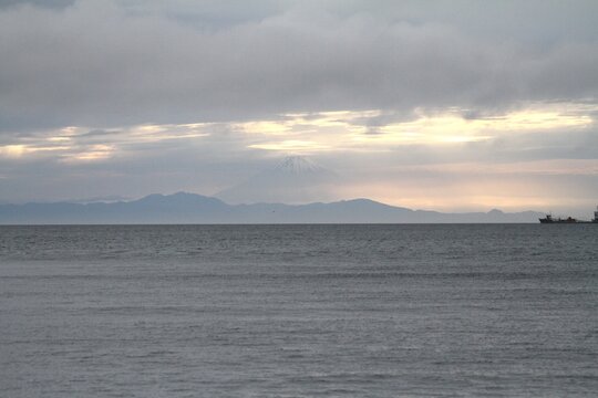 Horizontal wide scenic view of Mount Fuji silhouette under twilight clouds over the sea.