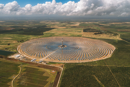 Aerial view of the Torresol Energy Gemasolar plant with its central tower and circular field of heliostat mirrors under a cloudy sky in Fuentes de Andalucia, Andalucia, Spain.
