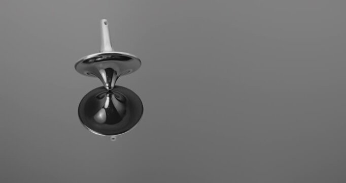 Metallic totem in initial steady rotation, gradually increasing wobble and tilt toward collapse against a mirrored backdrop.	