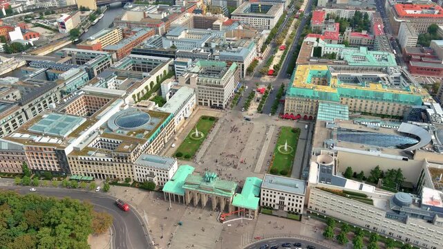 4K aerial view of Brandenburg Gate with quadriga statue and Pariser Platz with fountains, the iconic Hotel Adlon and Unter den Linden boulevard extending through Berlin Mitte.