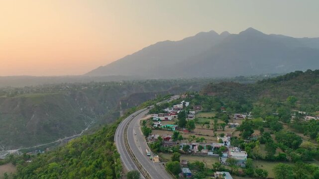 Drone shot of mountain road and Trikuta hills at golden hour. In the background, the majestic, hazy peaks of the Trikuta Hills&mdash;home to the holy Mata Vaishno Devi shrine.