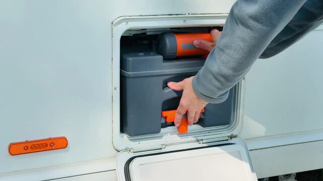 Woman hands removing a chemical toilet cassette from an RV utility compartment on a sunny day