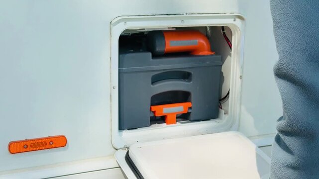 Woman hands inserting a clean chemical toilet cassette into an RV utility compartment outdoor