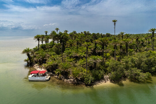 Aerial view of a lush tropical island with dense palm trees and people on a white boat with a red canopy moored on the shore Monrovia, Liberia.