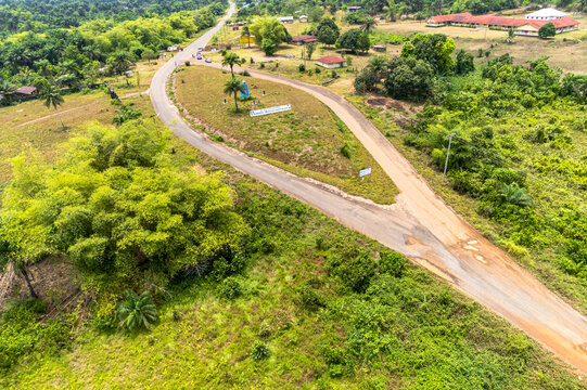 Aerial view of a road junction surrounded by lush tropical vegetation, small houses, and a red-roofed building under bright daylight in Monrovia, Liberia.