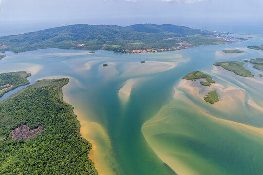 Aerial view of a coastal estuary featuring intricate sandbars, turquoise water, and lush green hills under a clear sky in Monrovia, Liberia.