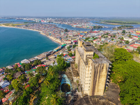 Aerial view of the abandoned Ducor Hotel on a hill overlooking the urban skyline, coastline, and Mesurado River under a clear blue sky in Monrovia, Liberia.
